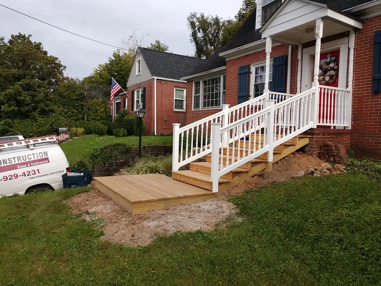 New pressure-treated wood steps and landing with white vinyl railings leading to the red front door of a brick house